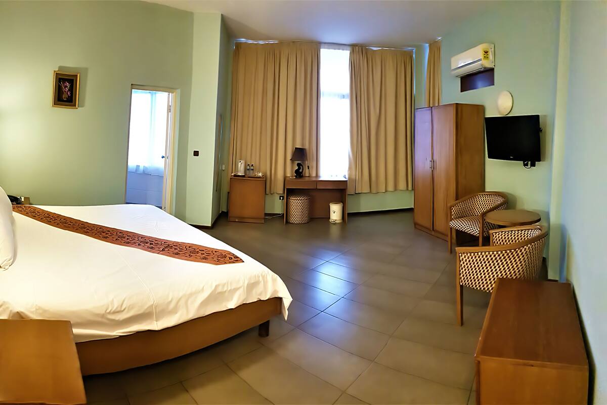 A hotel room with a bed, a desk, a chair, a wardrobe, and a television.