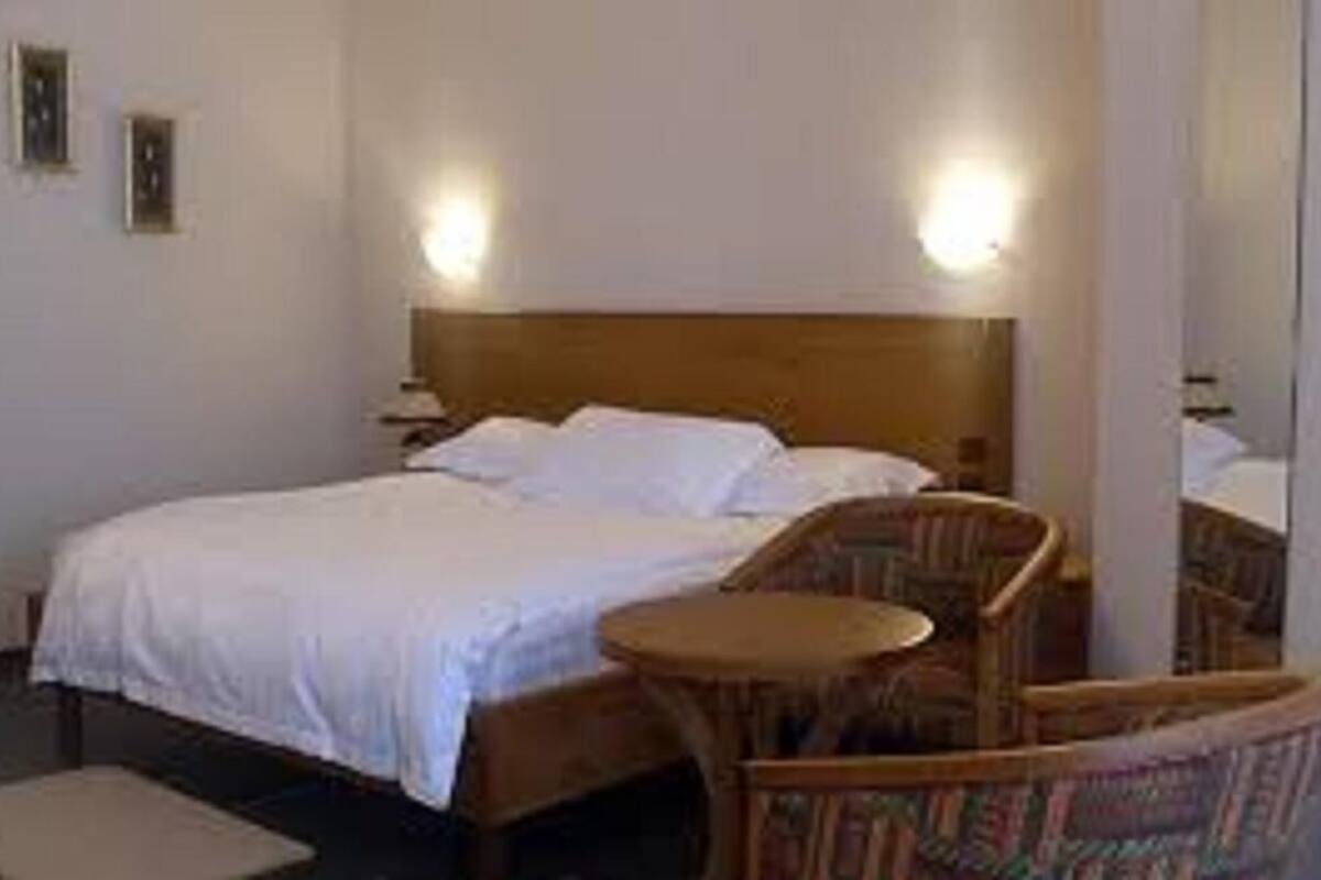 A hotel room with a bed, a chair, a small table, and two wall-mounted lamps.