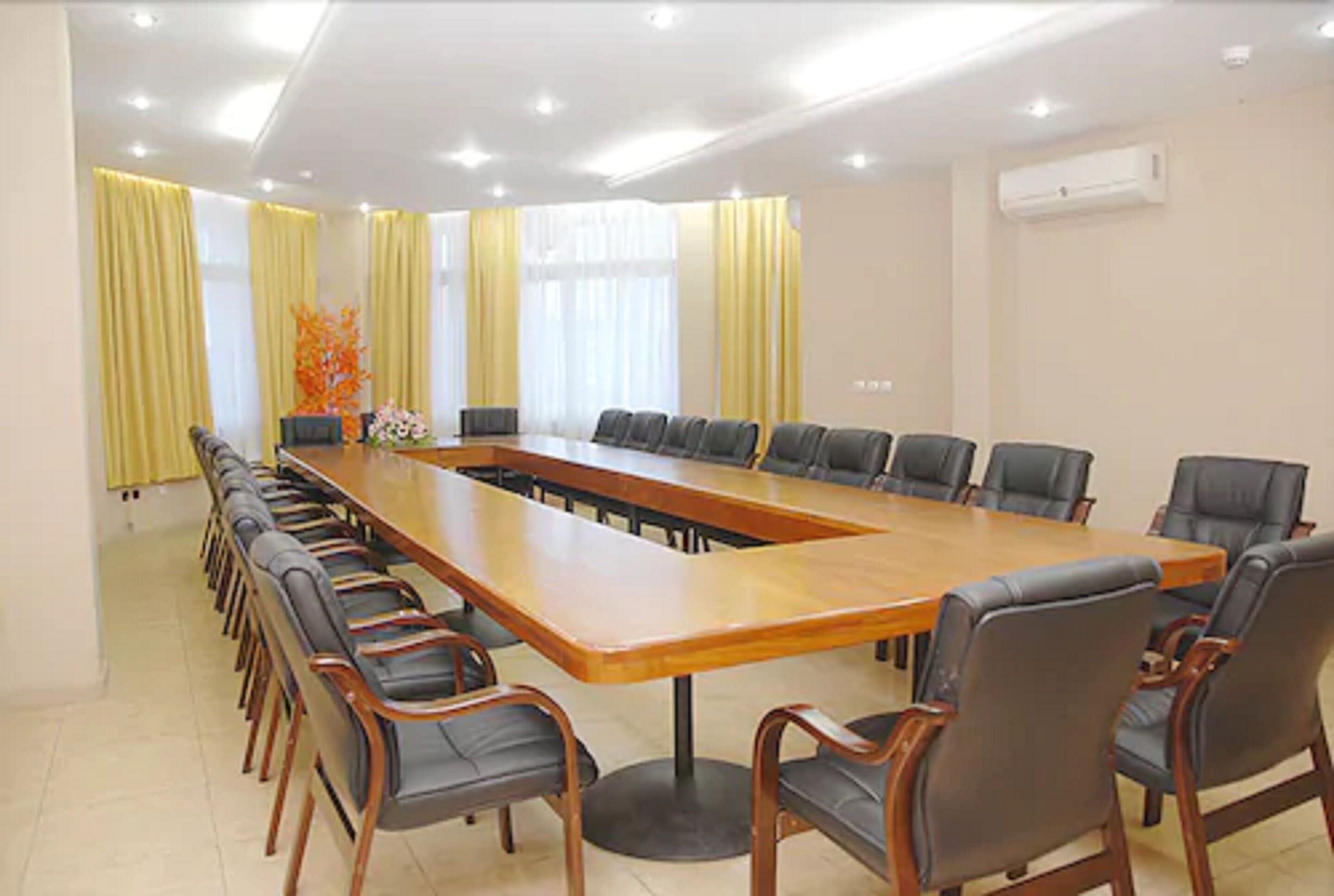 A conference room with a long table and chairs, yellow curtains, and an air conditioning unit on the wall.