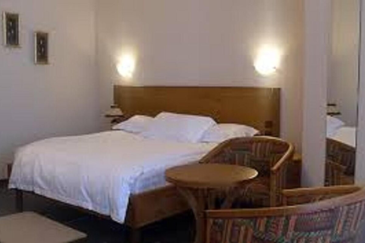 A hotel room with a bed, a chair, a small table, and two wall-mounted lamps.