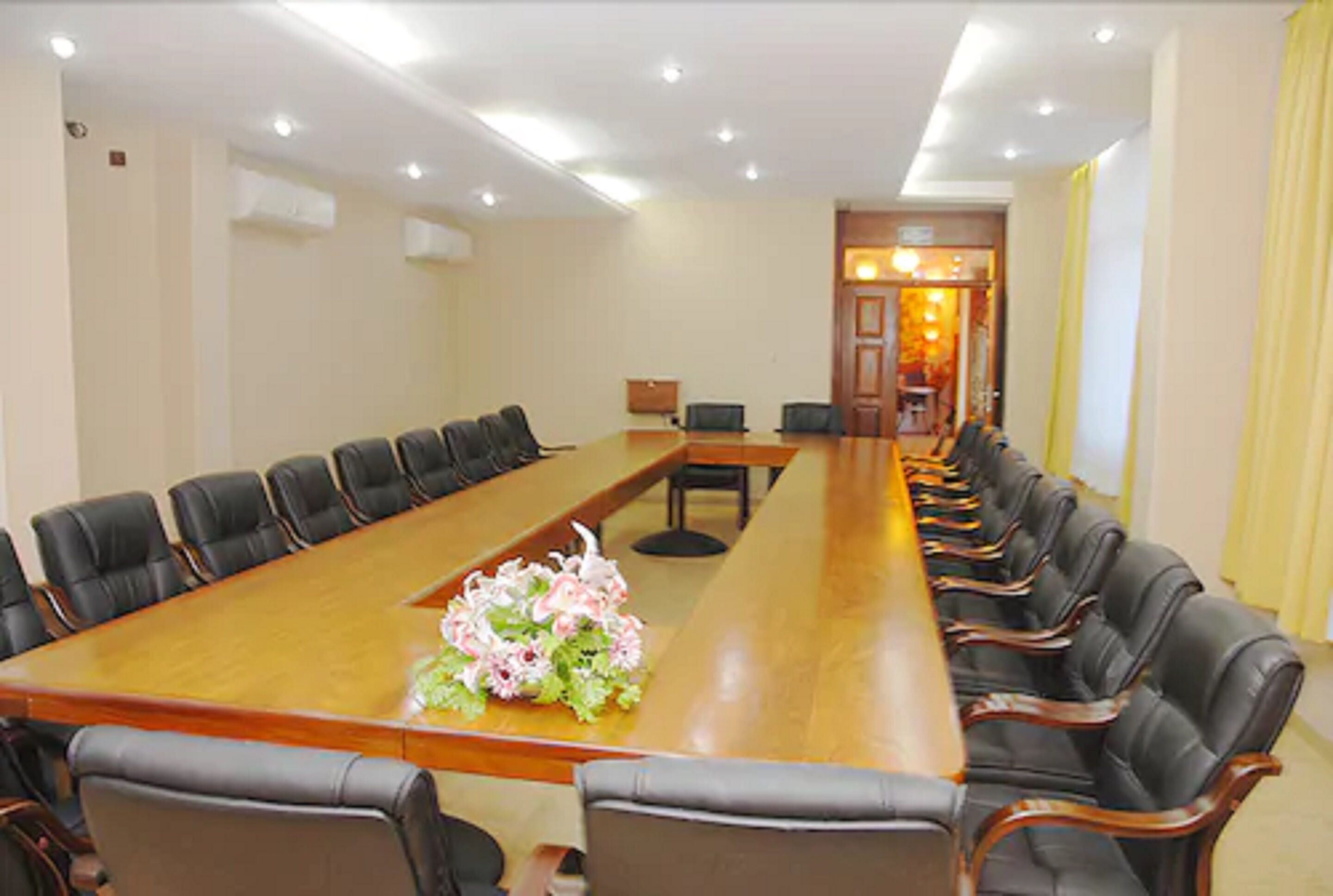 A conference room with a long table, black leather chairs, and a floral centerpiece.
