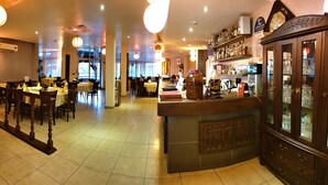 A restaurant interior with a bar area, dining tables, chairs, and a decorative cabinet with glassware. - Robinhood Inn (Accra)