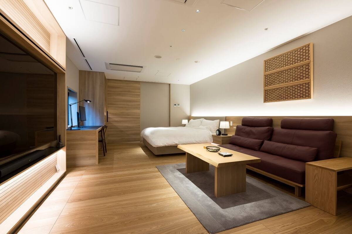 A modern hotel room with a bed, a sofa, a desk, and a TV.