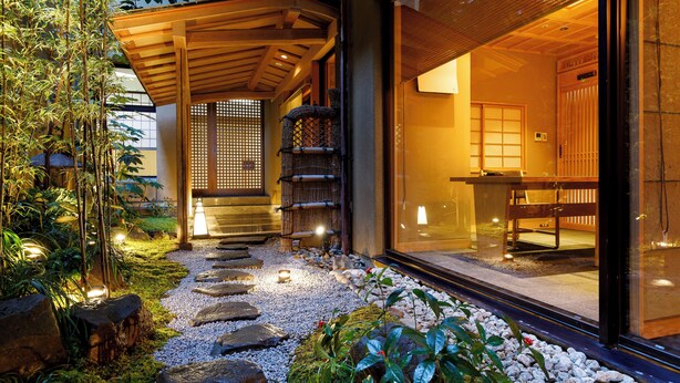 A traditional Japanese-style building with a wooden exterior, a stone pathway leading to a wooden entrance, and a view of the interior through large glass doors. - Arima Onsen Kinzan (Kobe)