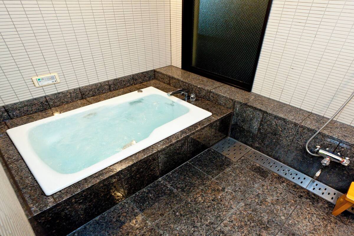 A modern bathroom with a large bathtub, granite countertops, a shower area, and a hand soap dispenser.