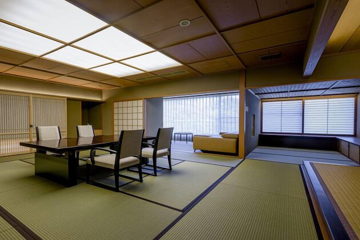 A traditional tatami mat room with a low table and chairs, sliding doors, and a view of the outside.