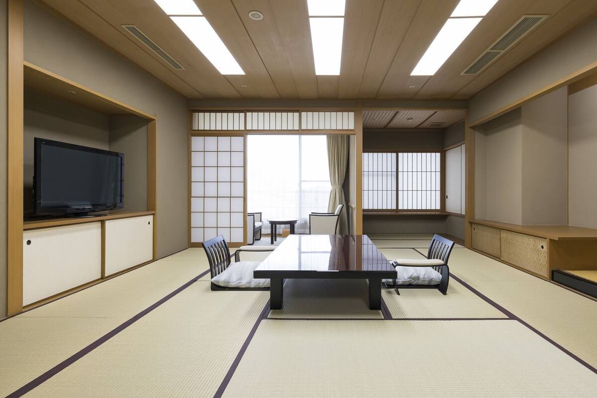 A traditional Japanese-style meeting room with tatami flooring, a central table, chairs, a television, and sliding doors.