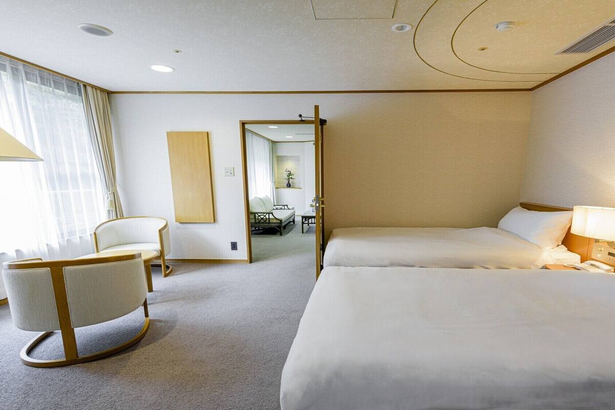 A hotel room with two beds, a sitting area with a chair, a desk, and a mirror.