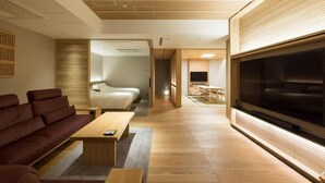 A modern hotel room with a large TV, a sofa, a dining area, and a wooden ceiling. - Arima Onsen Kinzan (Kobe)
