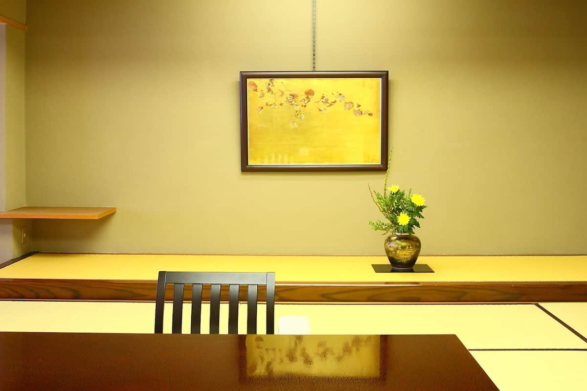 A room with a wooden table, a chair, a vase with flowers, and a framed picture on the wall.