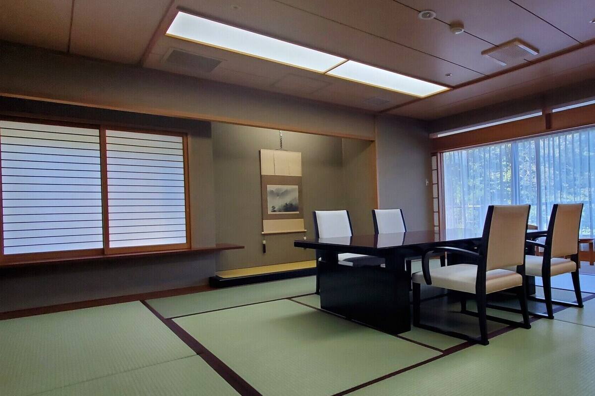 A traditional Japanese-style room with tatami flooring, a low table with chairs, and a large window with sheer curtains.