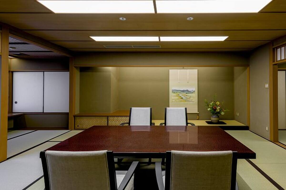 A conference room with a long table, chairs, a painting, and a vase with flowers.