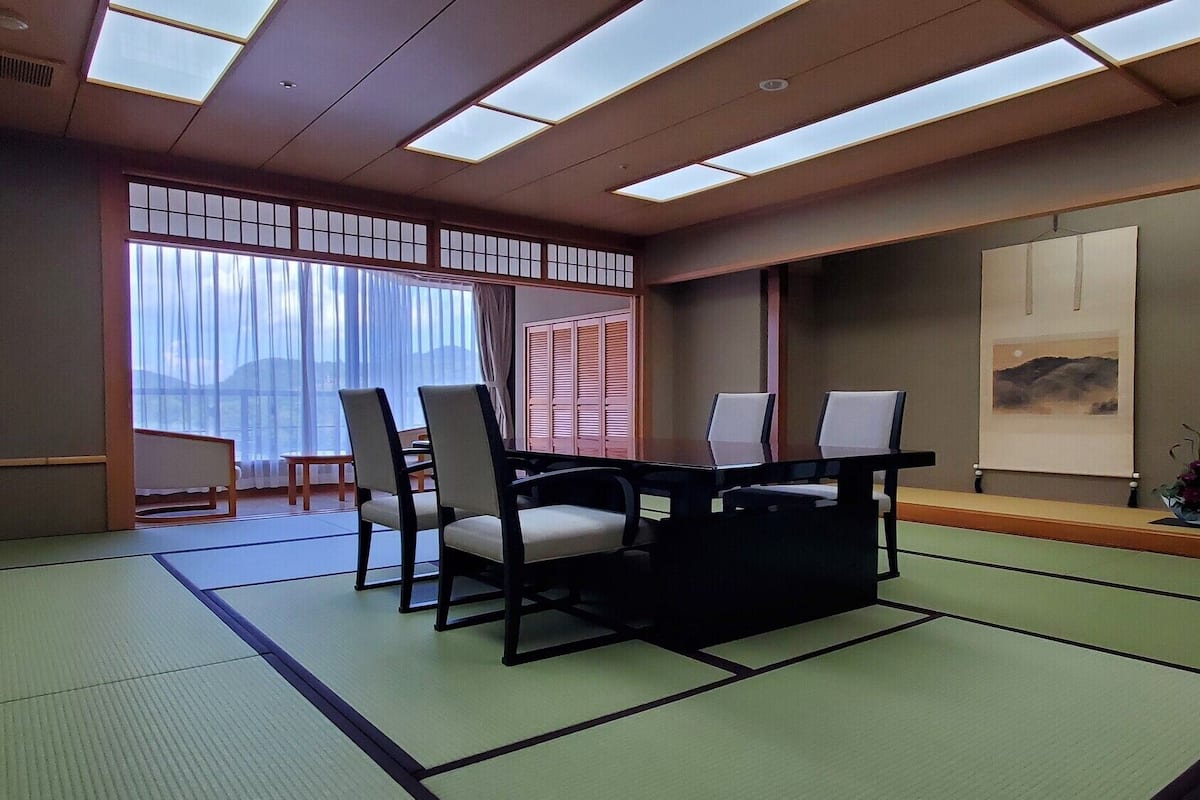 A tatami mat room with a low table, chairs, and a sliding door.