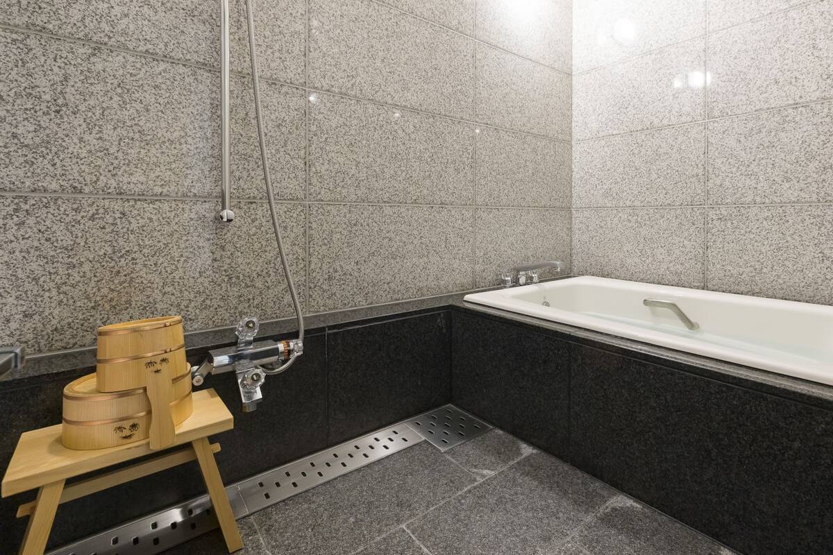 A modern bathroom with a bathtub, a shower, and a wooden stool with containers.
