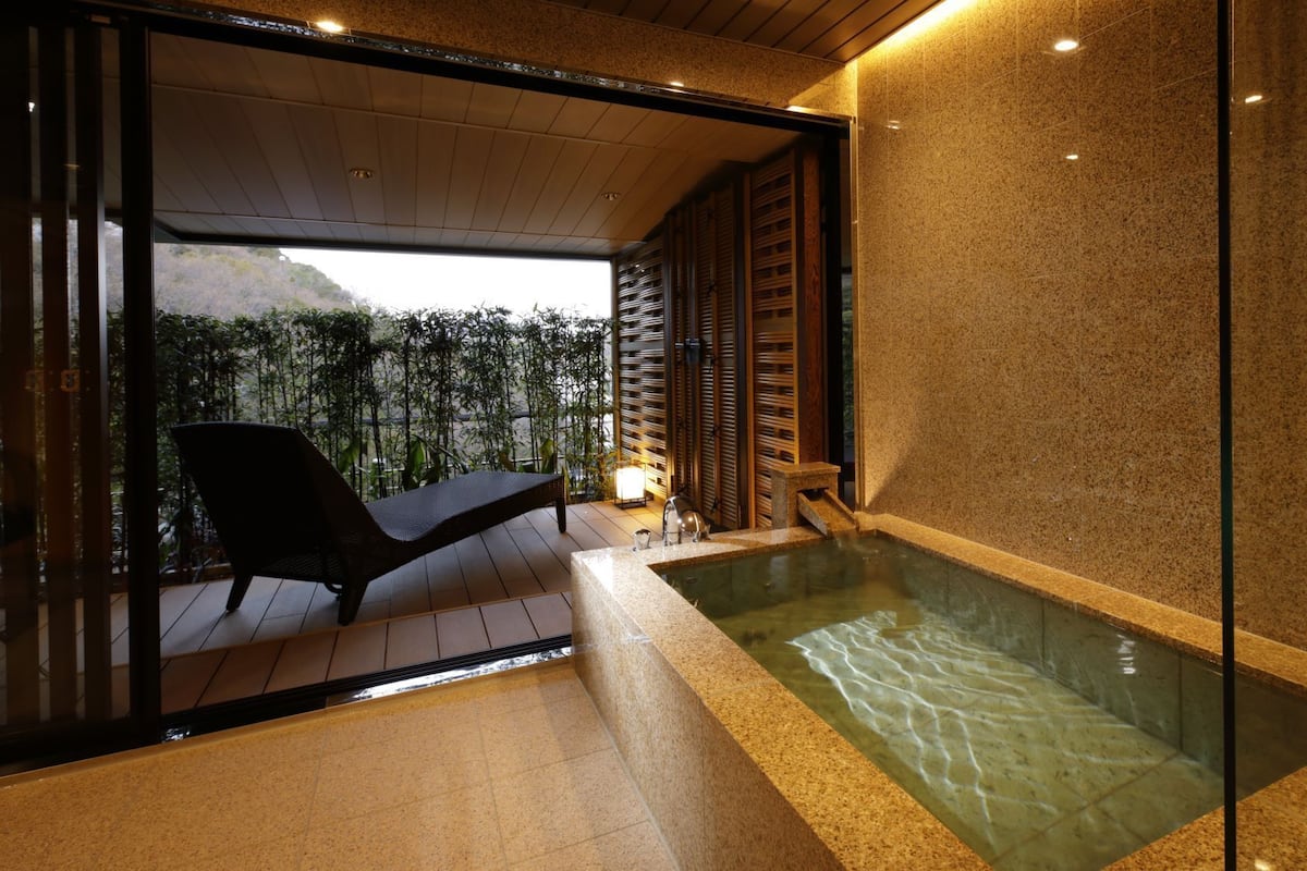 A modern spa area with a glass-enclosed hot tub, a lounge chair, and a view of a mountainous landscape.
