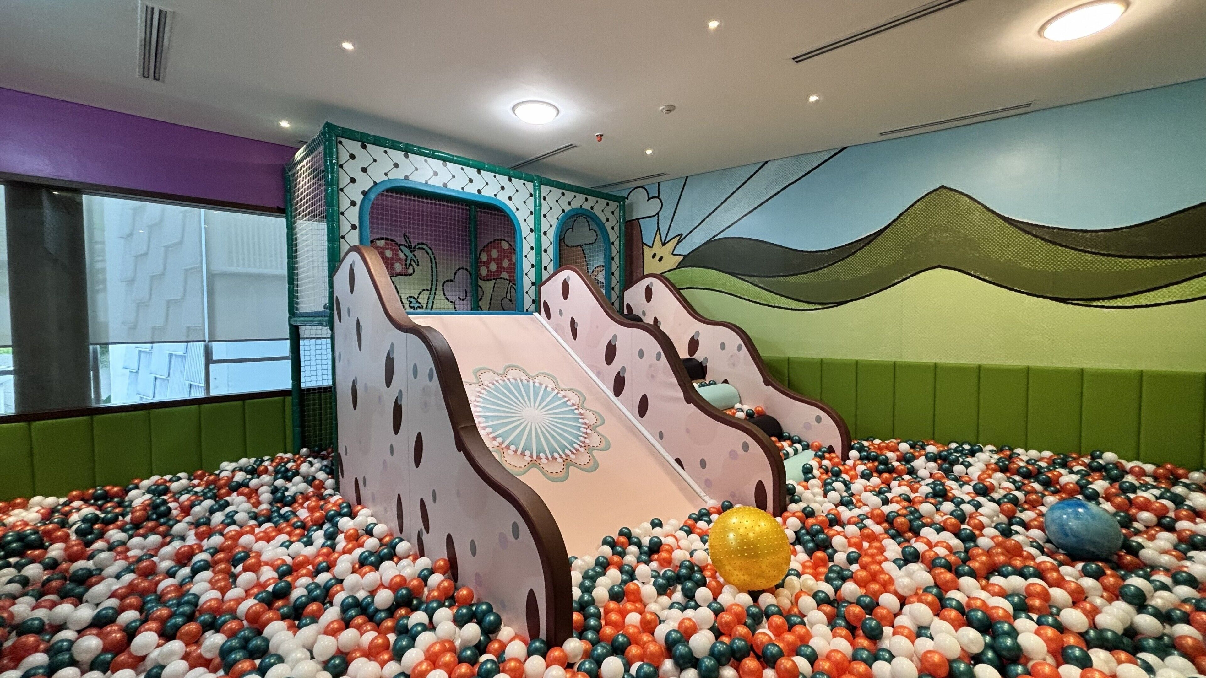 A play area with a ball pit, slides, and a mural.