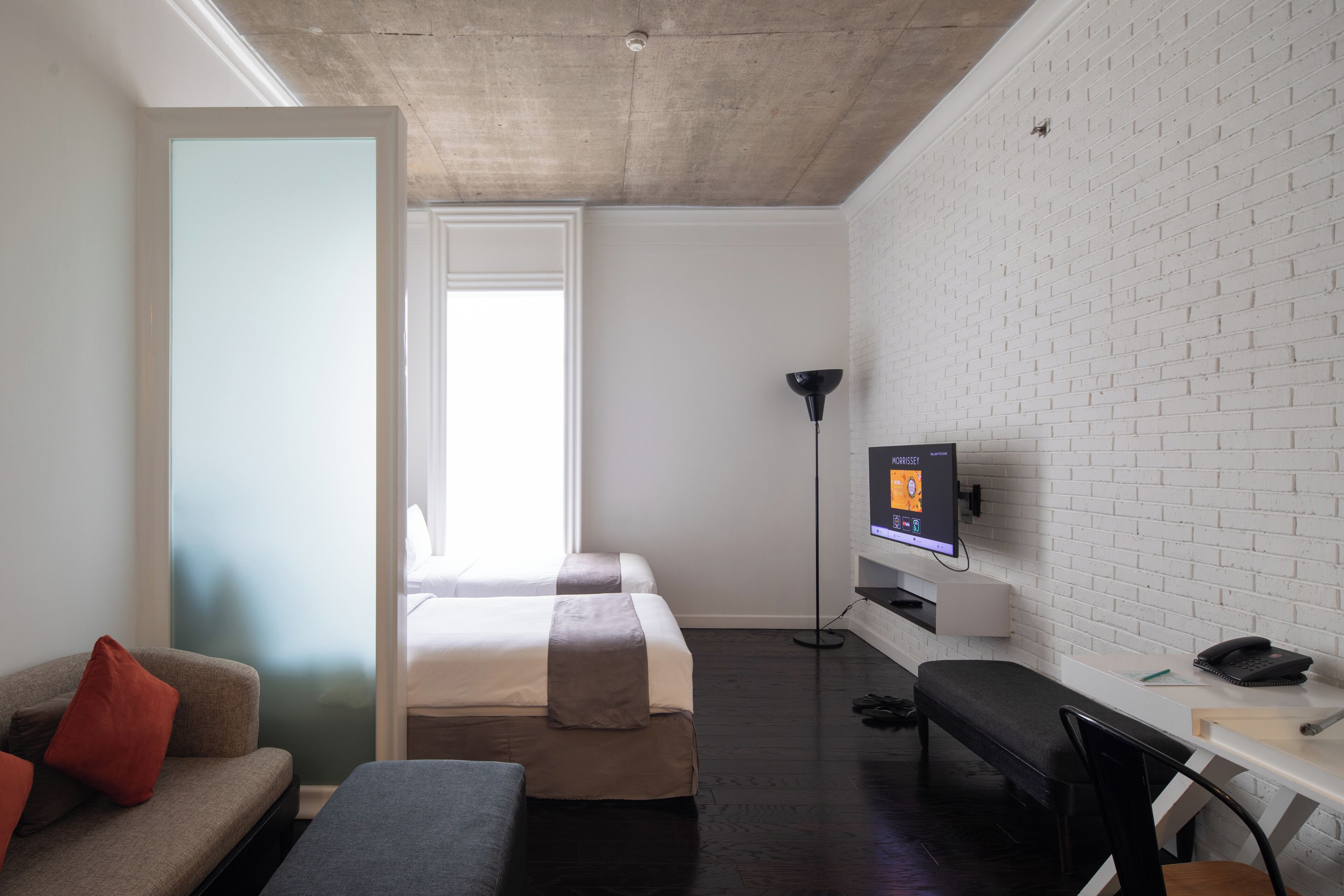 A modern hotel room with a bed, a desk, a chair, a TV, and a couch.