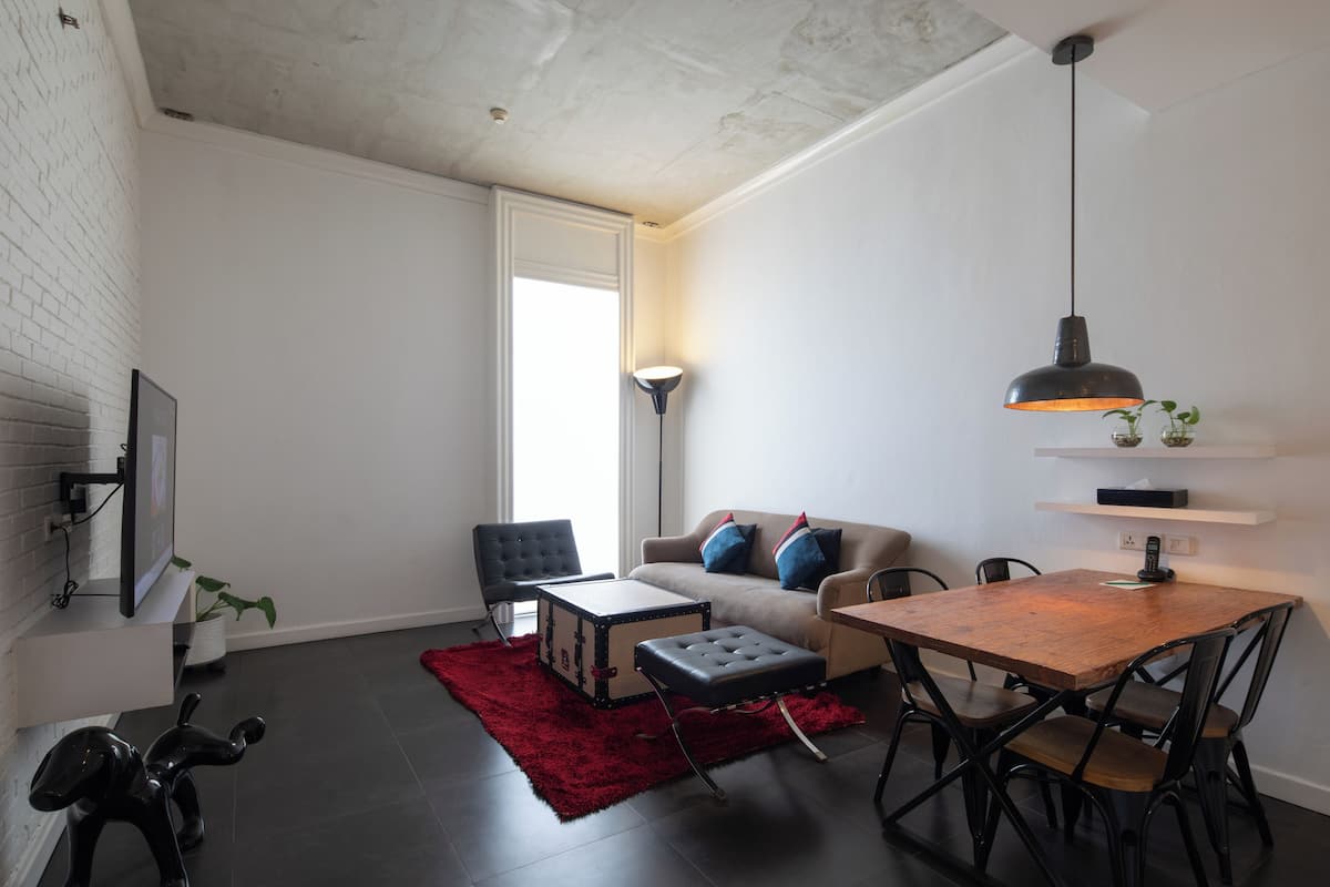 A modern living room with a sofa, a dining table, and a red rug.