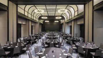 A large conference room with multiple round tables, each surrounded by chairs, and a high ceiling with decorative lighting.