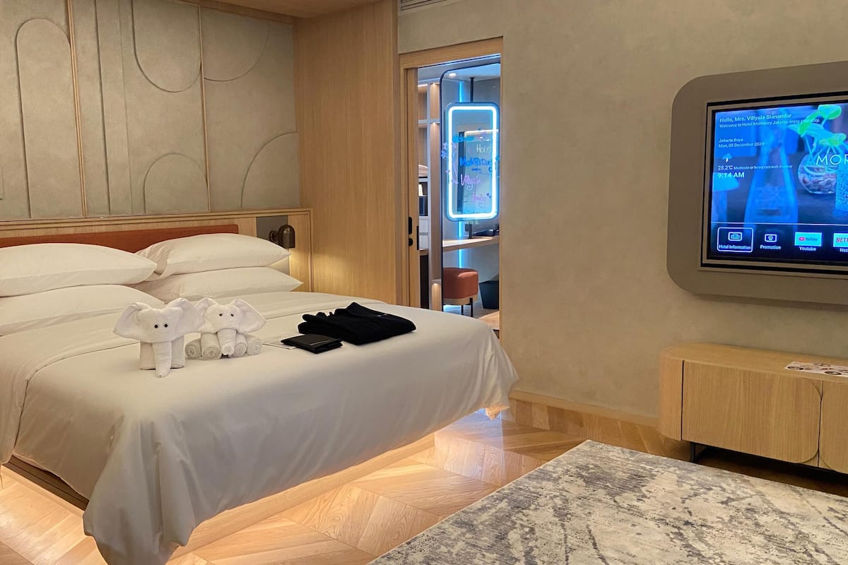 A hotel room with a bed, a TV, and a wooden floor.