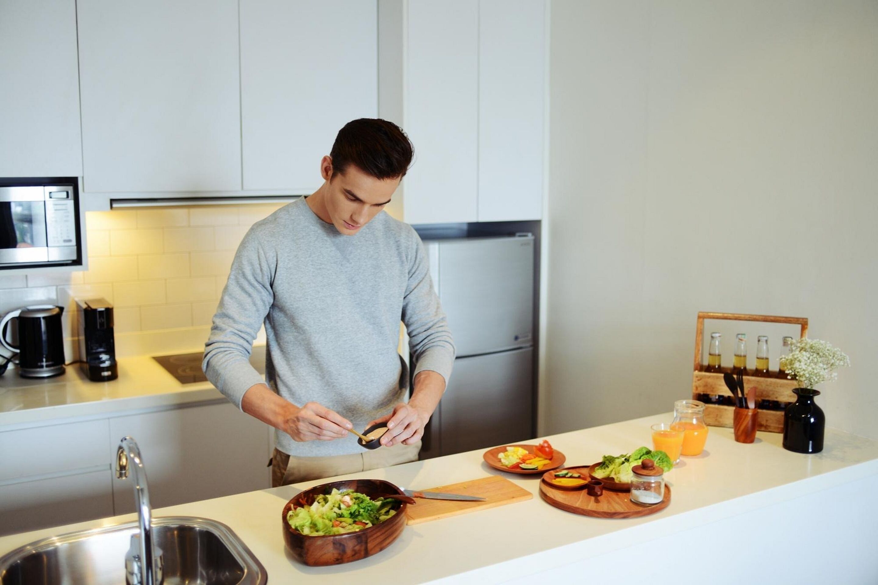 A modern kitchen with white cabinets, a stainless steel sink, a microwave, and a refrigerator.