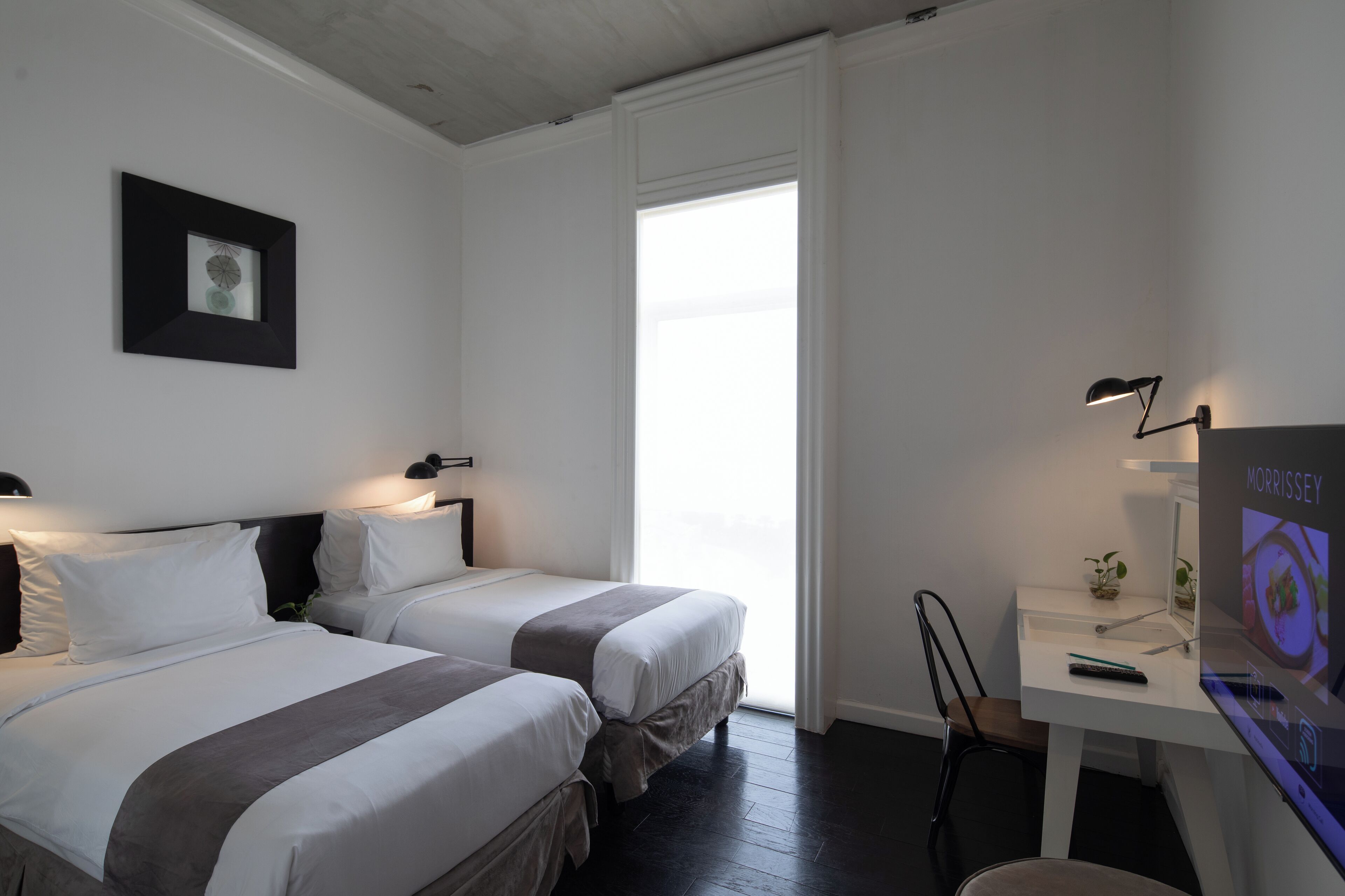 Habitación de hotel con dos camas, un escritorio y un televisor mostrando 'MORRISSEY'.