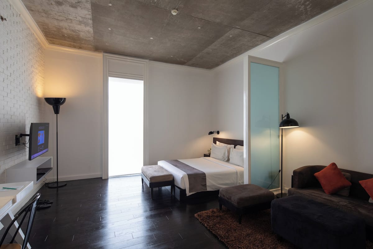 A modern hotel room with a large bed, a desk, a chair, a sofa, and a TV.