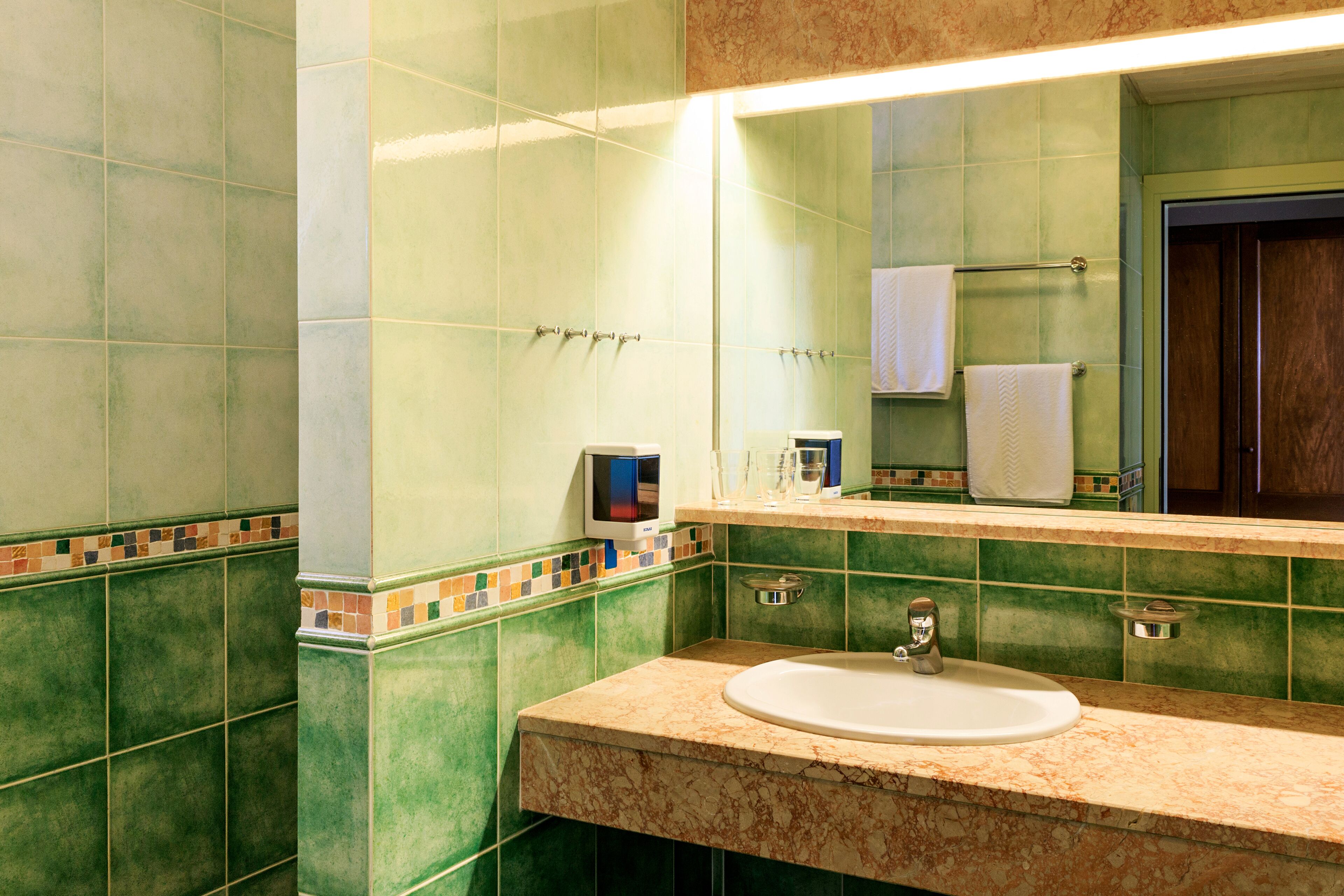 Een badkamer met groene tegels, een wastafel, een spiegel en een handdoekhouder.