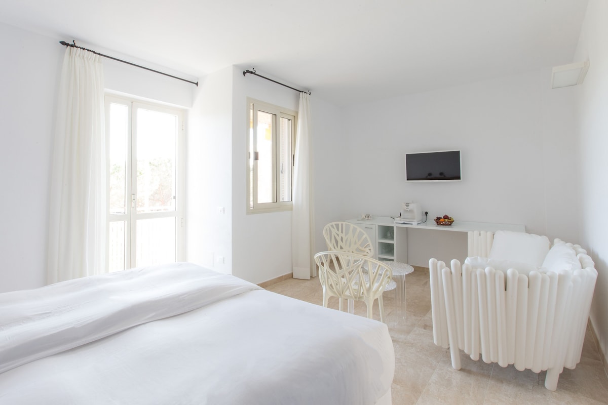 A hotel room with a bed, a desk, a chair, and a radiator.
