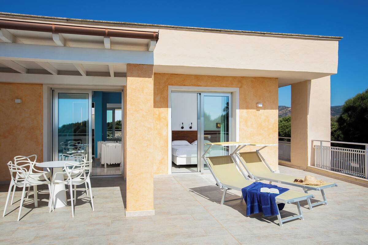 A modern outdoor patio with a dining area, lounge chairs, and a bedroom with a sliding glass door.