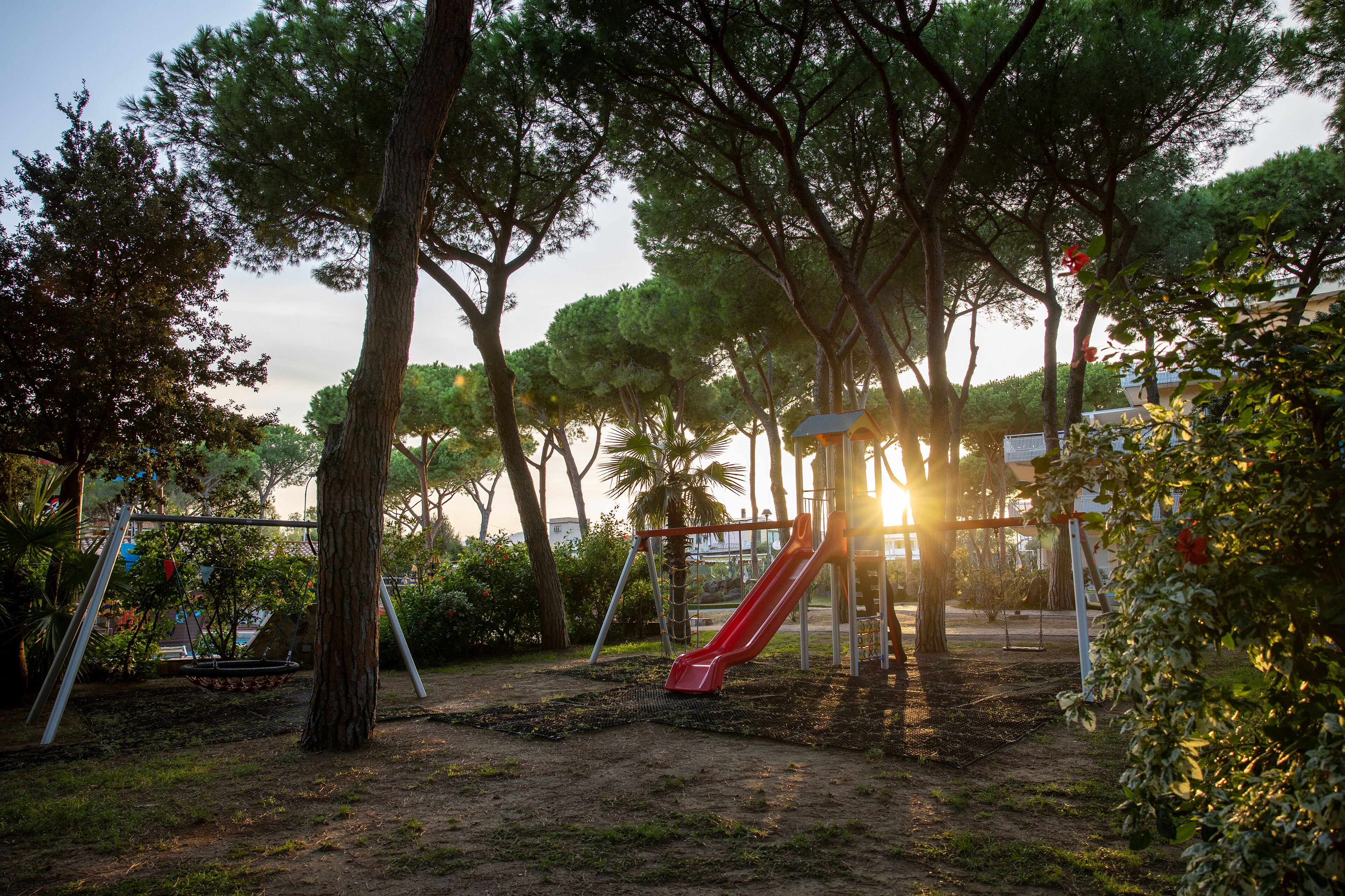 A playground with a red slide and swings, surrounded by trees and a fence.