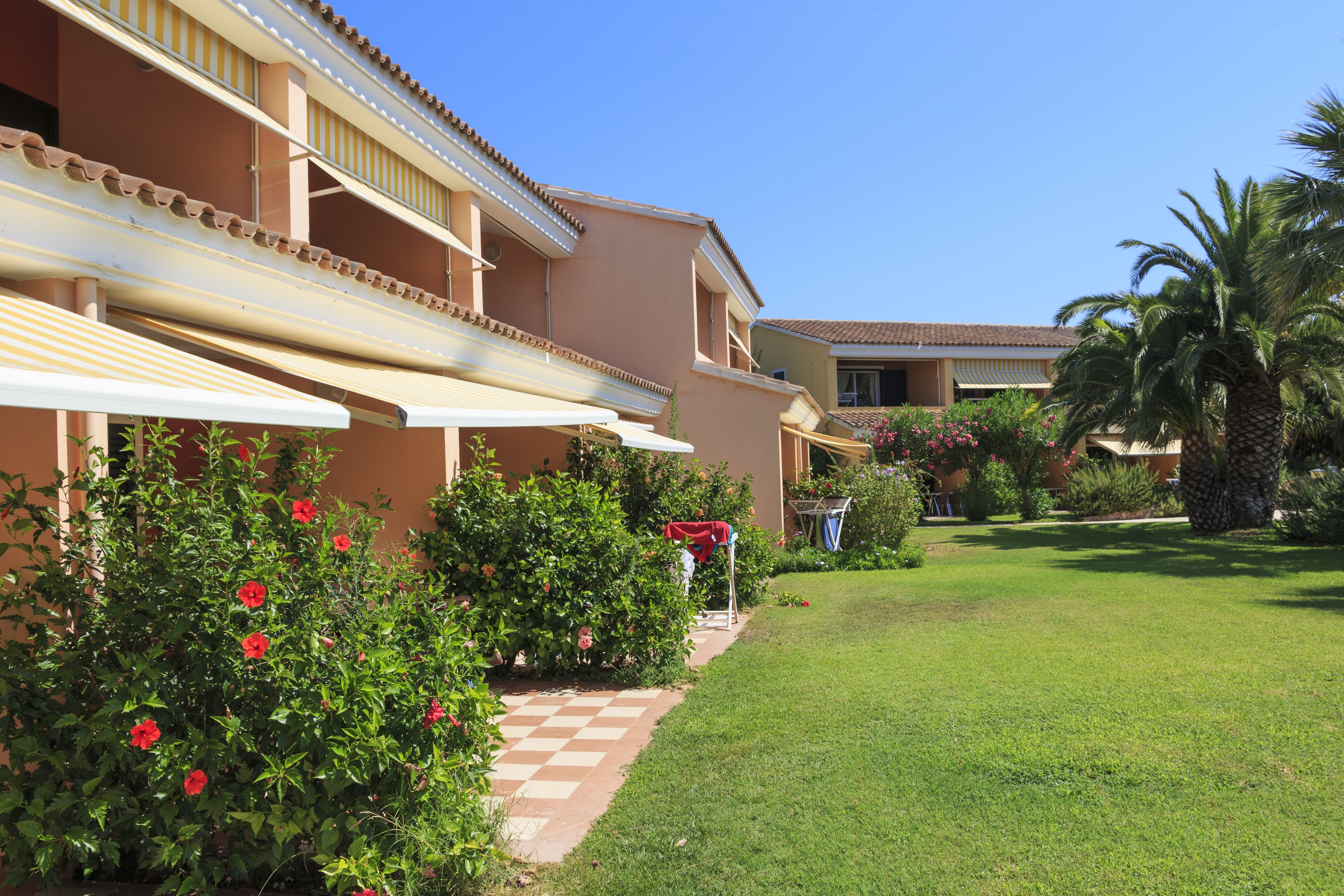 Un hotel con un vialetto a scacchi che conduce all'ingresso, circondato da rigogliosa vegetazione e palme.
