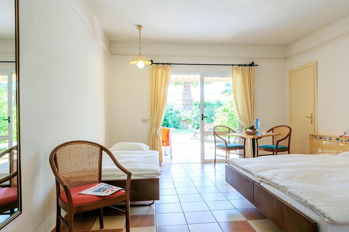 A hotel room with a bed, a chair, a table with a basket, and a view of the outdoors.