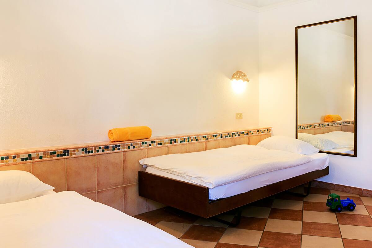 A hotel room with two beds, a tiled floor, a wall-mounted mirror, and a small toy car on the floor.