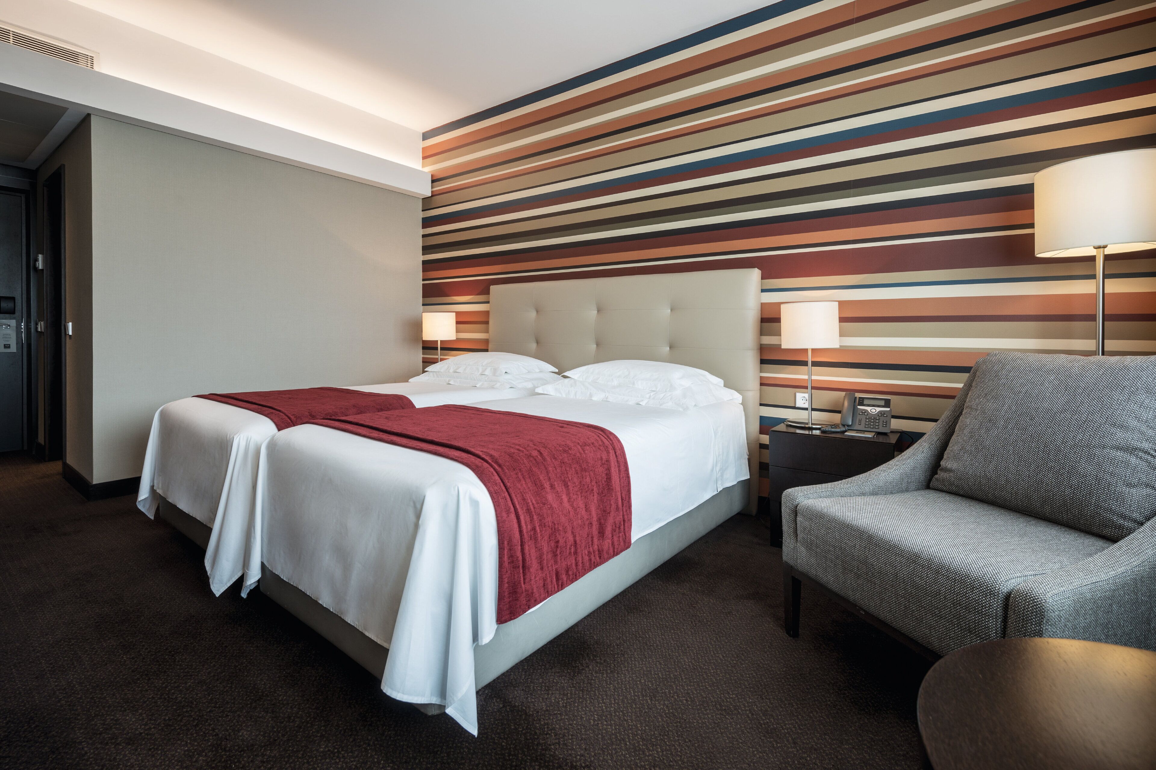 Una habitación de hotel con una cama, una silla y una pared a rayas.