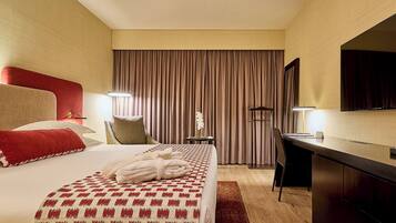 Habitación de hotel con cama, escritorio, silla, televisor y ventana con cortinas.