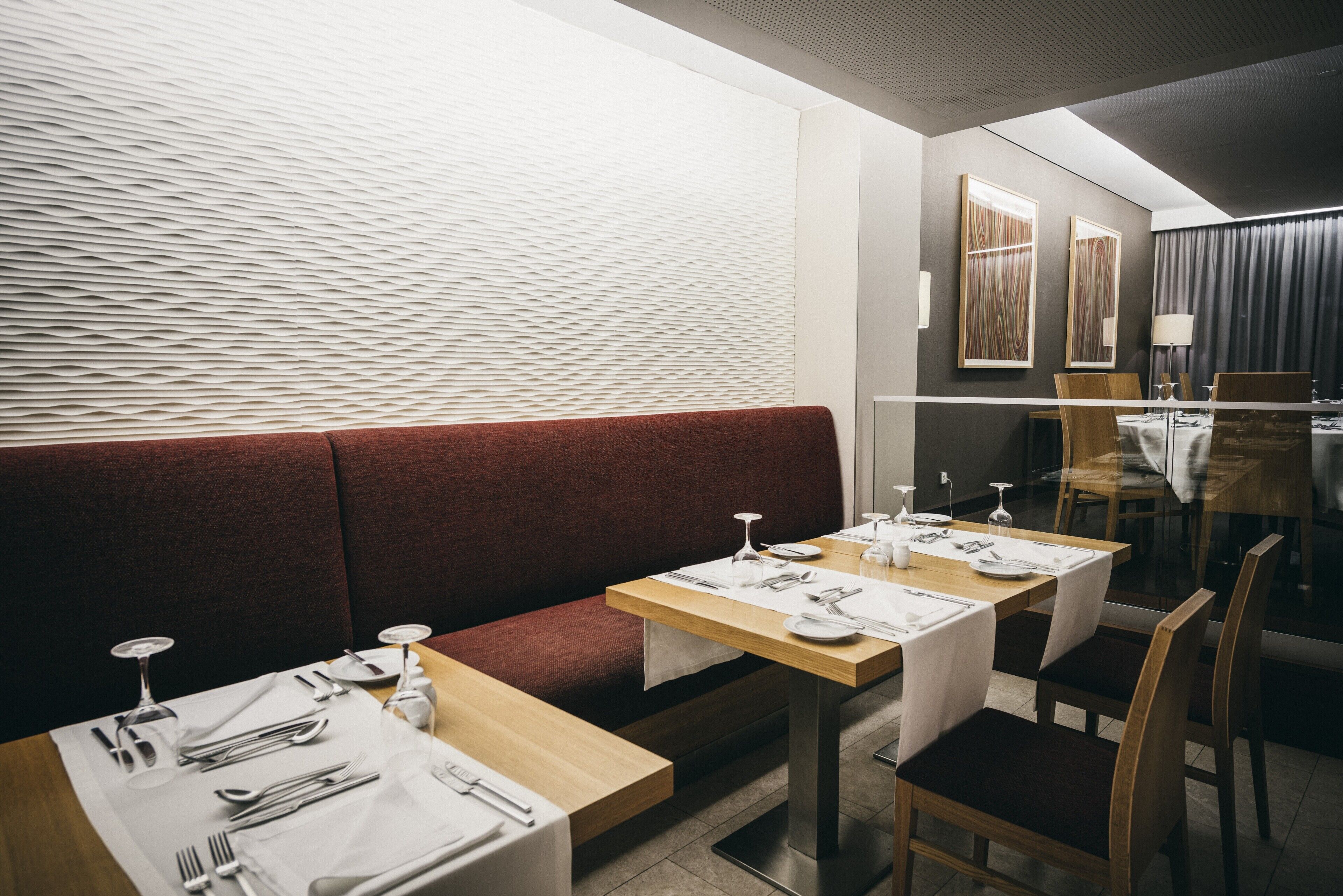 Un restaurante con un banco acolchado rojo, mesas de madera y manteles blancos.