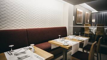 Un restaurante con un banco acolchado rojo, mesas de madera y manteles blancos.