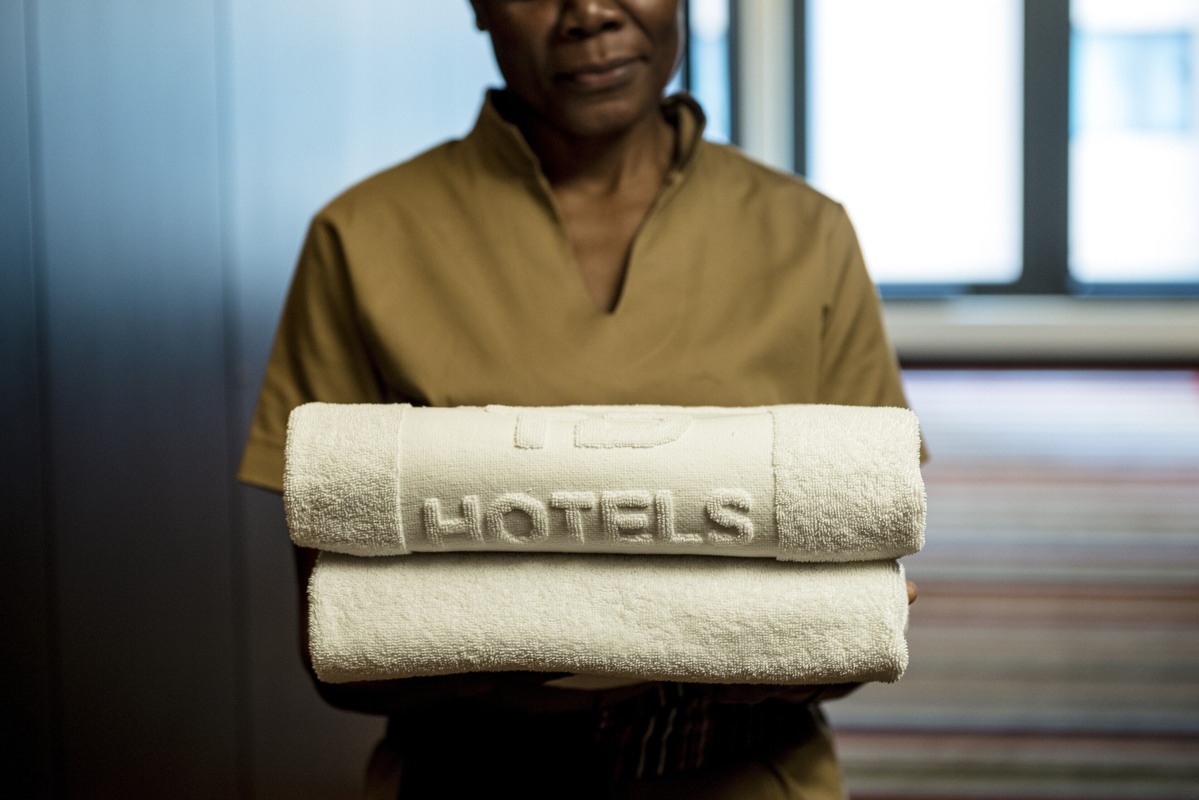 Una persona sostiene una pila de toallas blancas con la palabra 'HOTELS' en relieve.