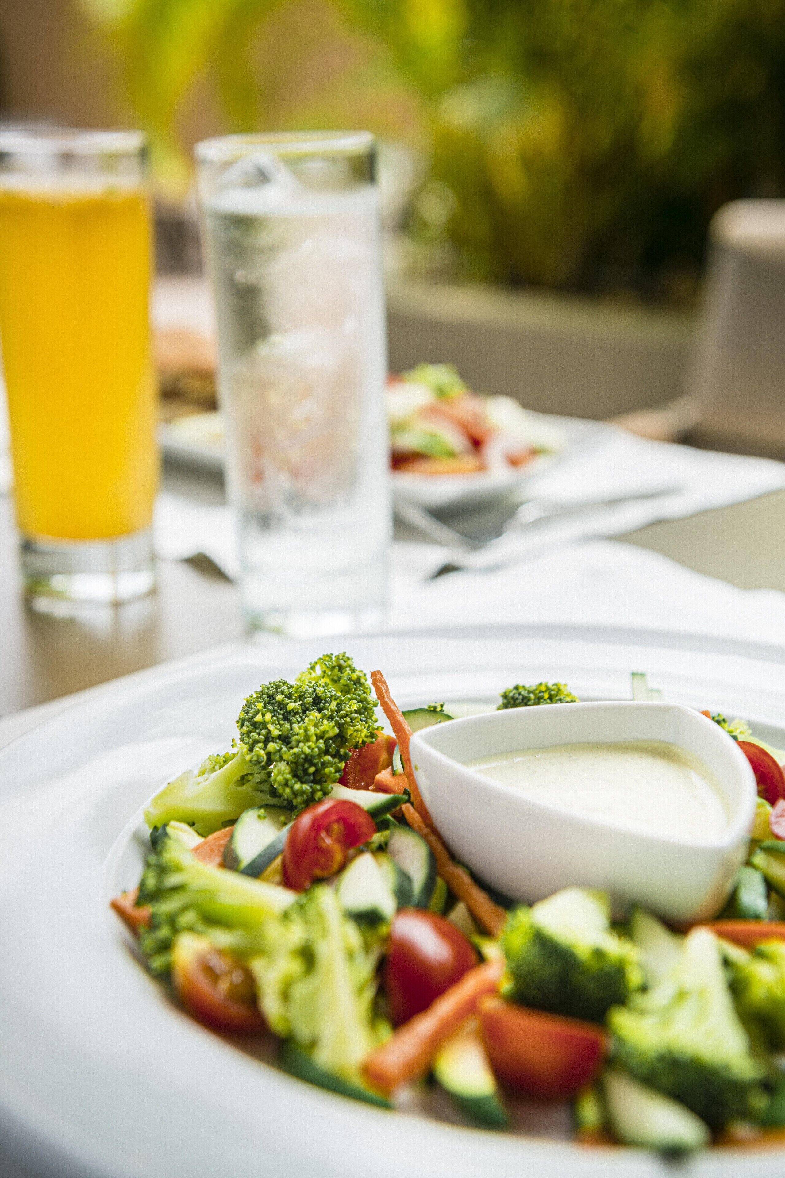 A plate of mixed vegetables with a side of dipping sauce, a glass of orange juice, and a glass of water on a table.