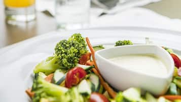 A plate of mixed vegetables with a side of dipping sauce, a glass of orange juice, and a glass of water on a table.