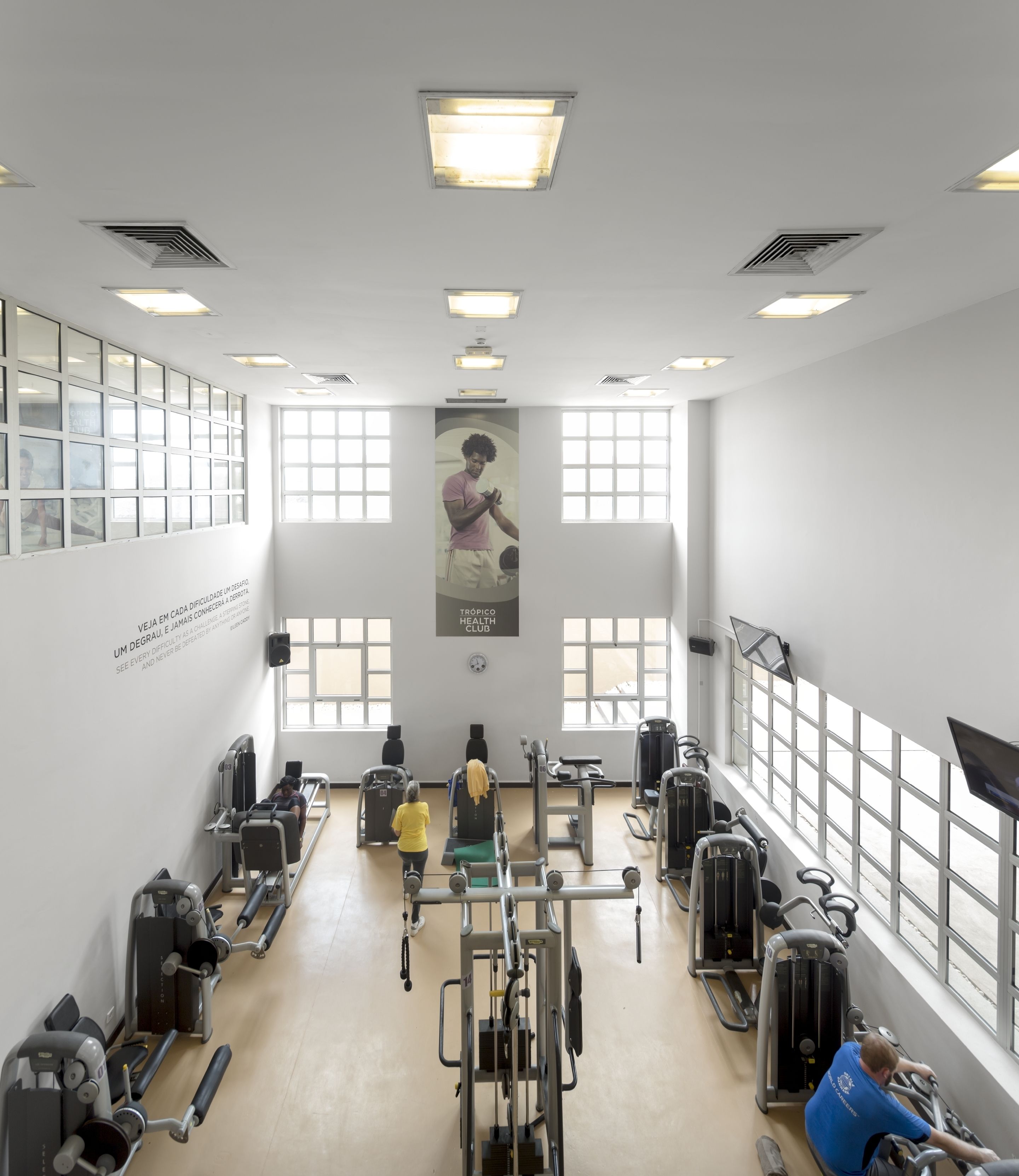 A gym with various exercise machines, large windows, and a motivational poster on the wall.