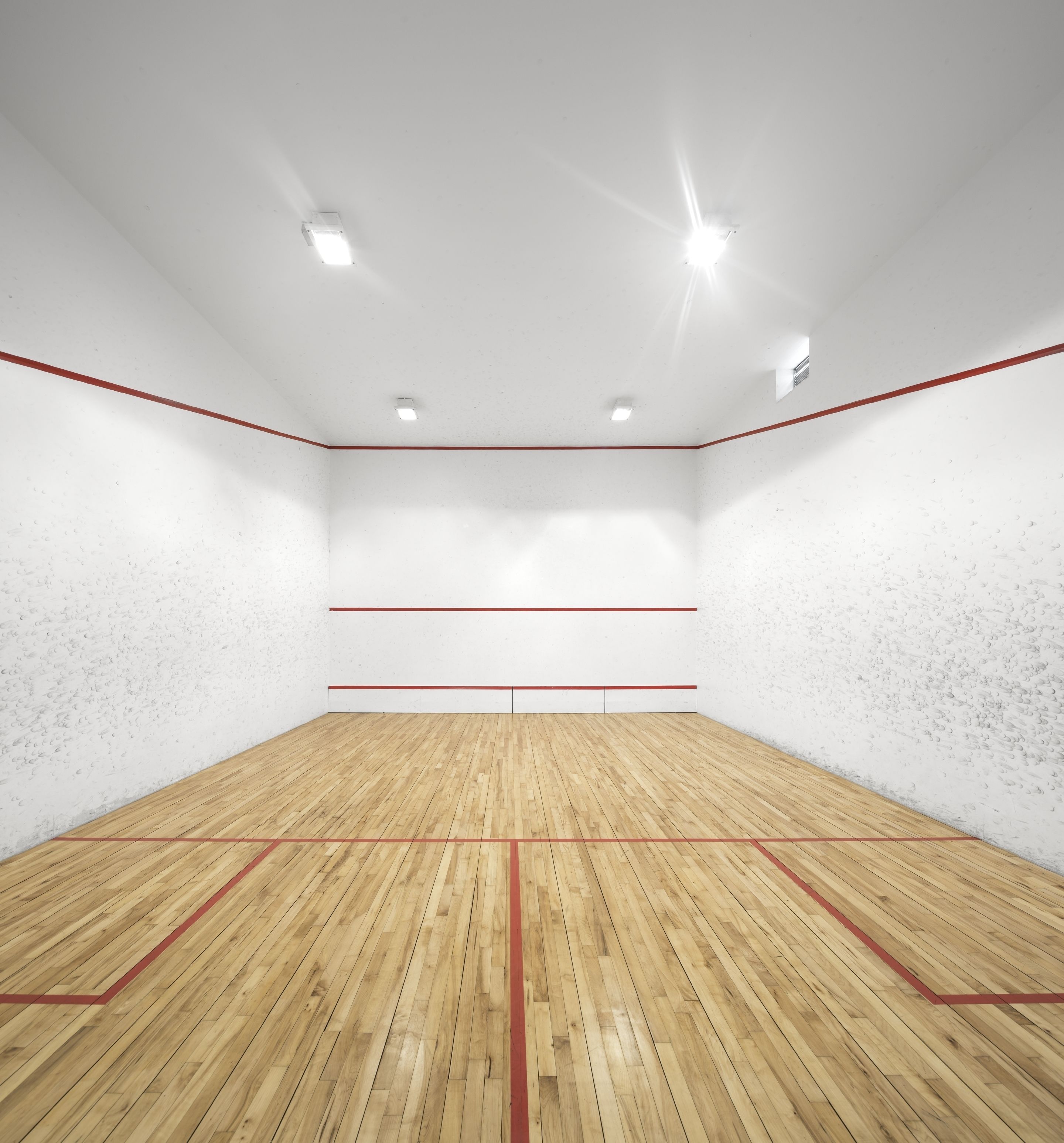 A squash court with wooden flooring and red lines marking the playing area.