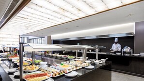 A buffet setup with various food items and a chef in the background. - Hotel Trópico (Luanda)