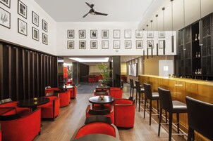Un espace bar moderne avec des sièges rouges, un comptoir en bois et des tableaux encadrés aux murs.