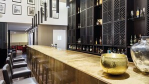 A bar area with a long counter, black leather bar stools, and a decorative gold bowl. - Hotel Trópico (Luanda)