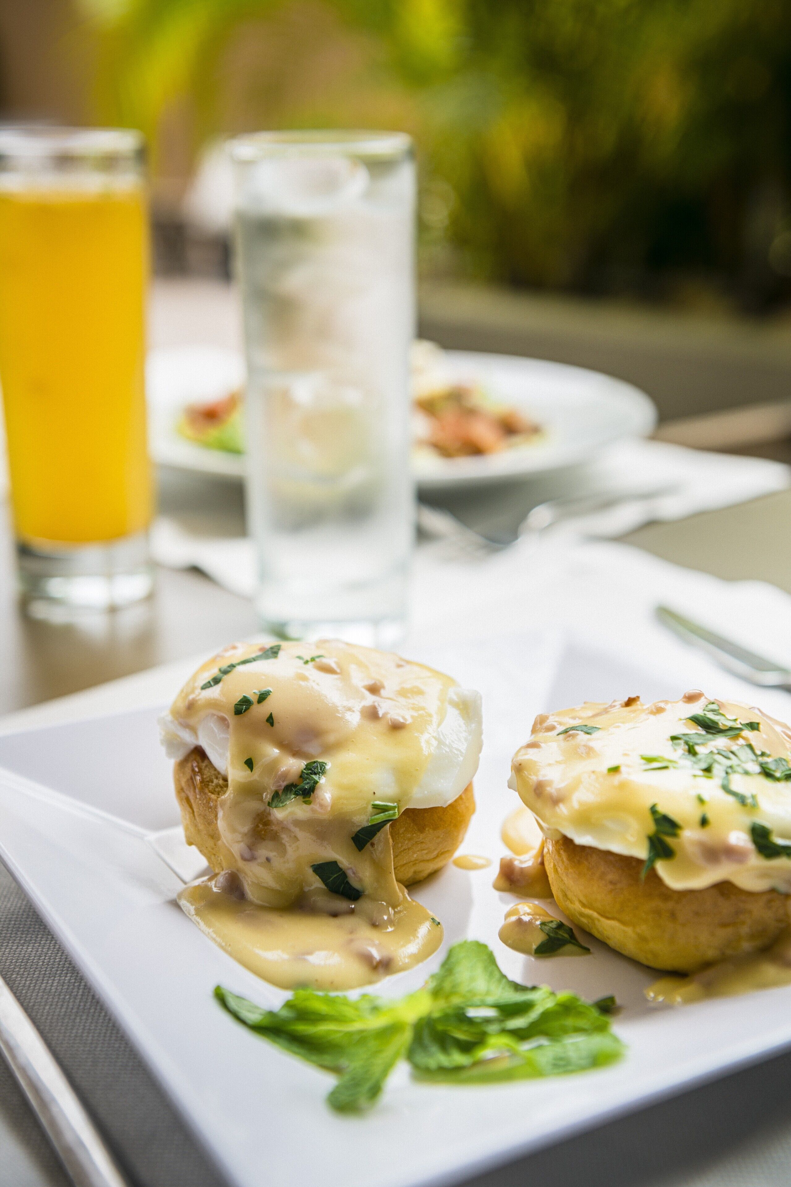 Disposição de mesa para o café da manhã, com ovos benedict e um copo de suco de laranja.
