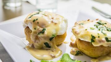 Disposição de mesa para o café da manhã, com ovos benedict e um copo de suco de laranja.
