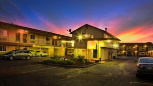 Un motel composé d’un bâtiment principal et de plusieurs unités attenantes, doté d’un parking et offrant une vue sur le ciel au coucher du soleil.