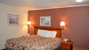 Une chambre d’hôtel avec un grand lit, deux lampes de chevet, une table de chevet, une chaise et deux tableaux encadrés au mur.